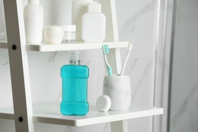 Photo of Bottle of mouthwash, toothbrushes and dental floss on white shelf in bathroom