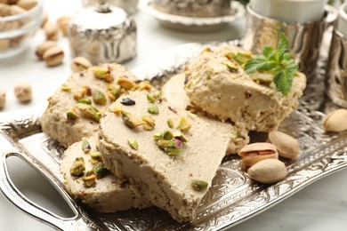 Photo of Tasty halva with pistachios and mint on white table, closeup