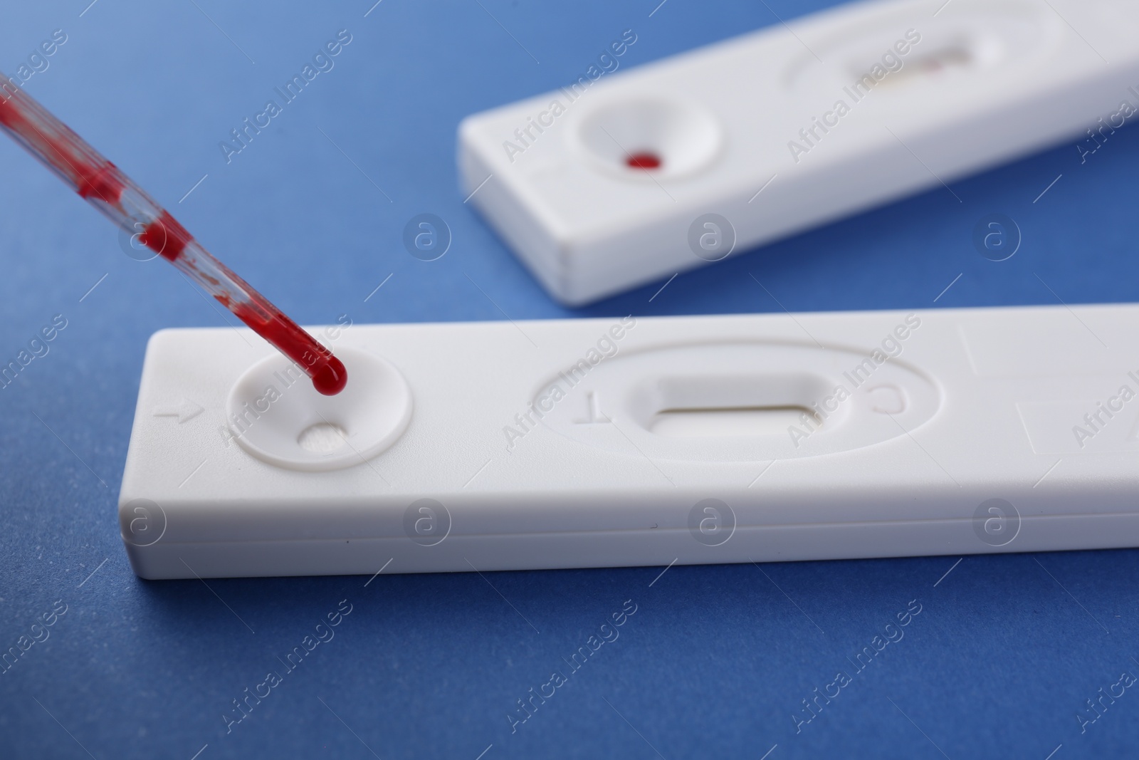 Photo of Dropping blood sample onto disposable express test cassette with pipette on blue background, closeup