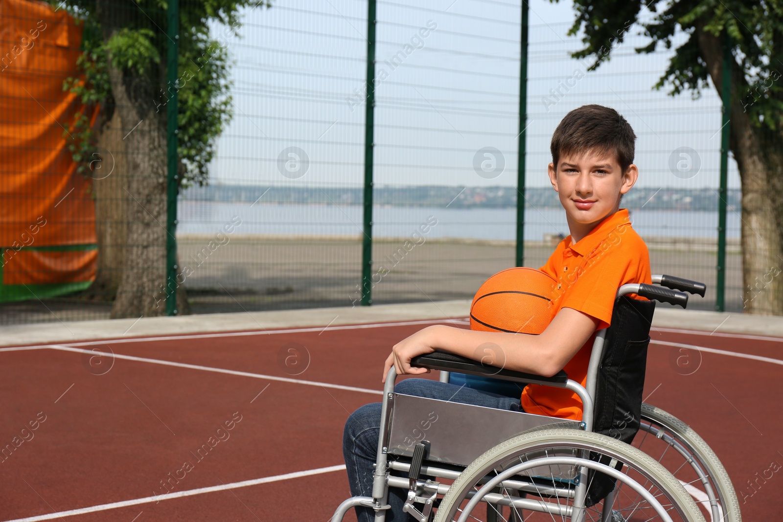 Photo of Disabled teenage boy in wheelchair with basketball ball at outdoor court