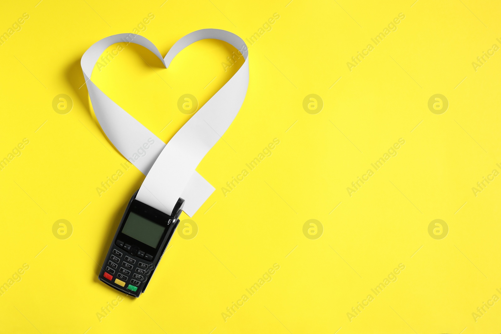 Photo of Payment terminal and heart made of thermal paper for receipt on yellow background, top view. Space for text