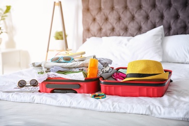 Photo of Open suitcase with different clothes and accessories for summer journey on bed