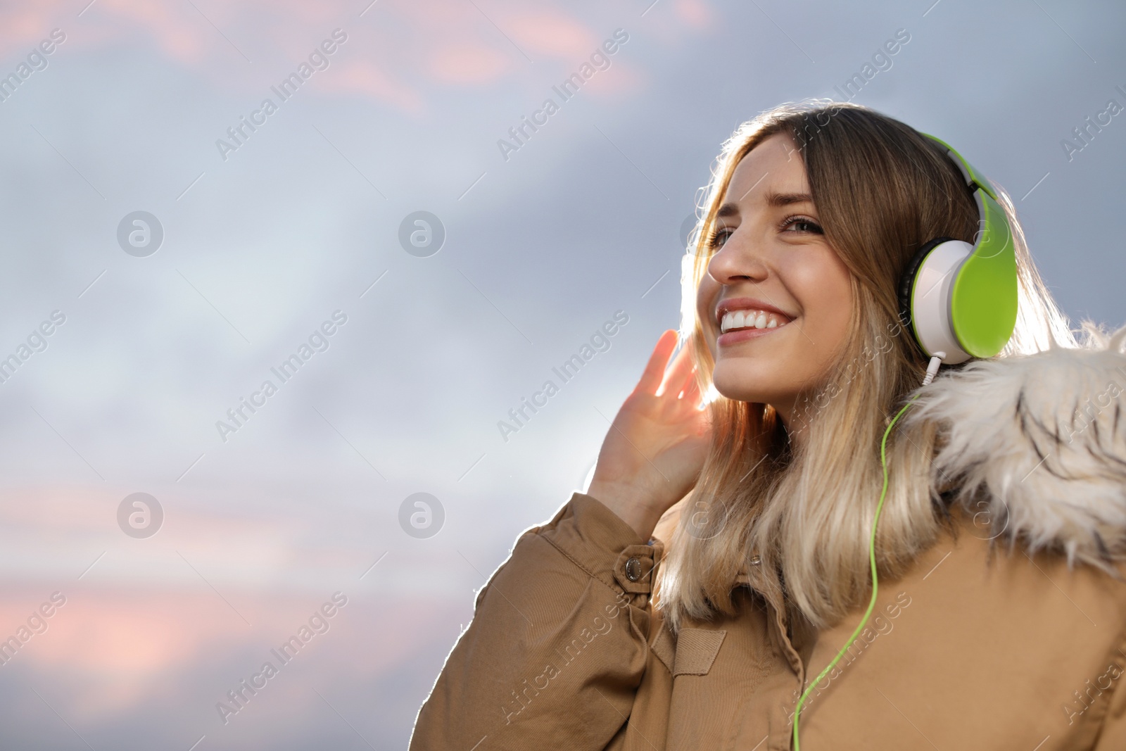 Photo of Young woman with headphones listening to music outdoors, space for text