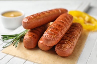 Delicious grilled sausages on white wooden table, closeup. Barbecue food