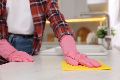 Photo of Woman cleaning white marble table with microfiber cloth in kitchen, closeup