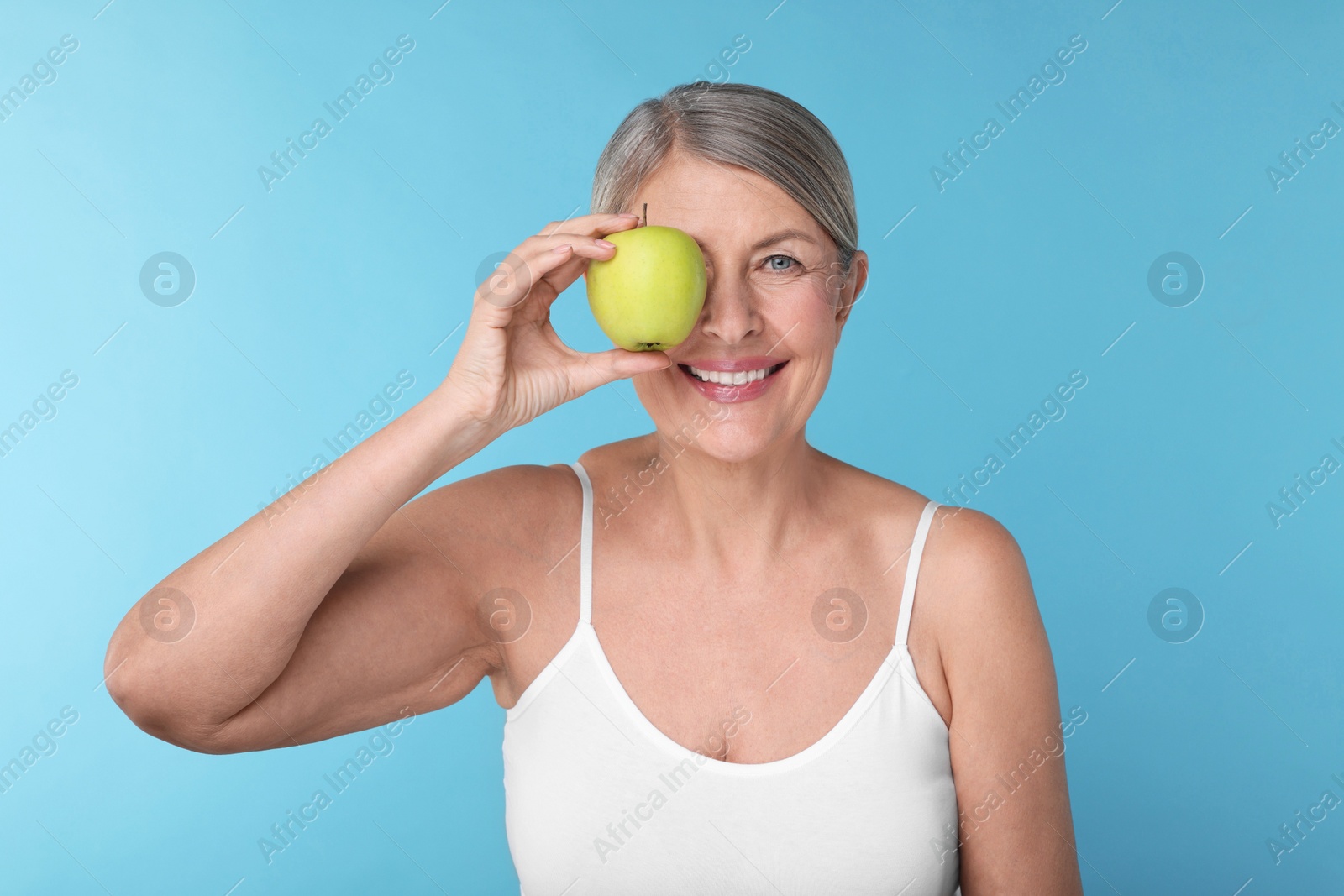 Photo of Beautiful woman with fresh apple on light blue background. Vitamin rich food