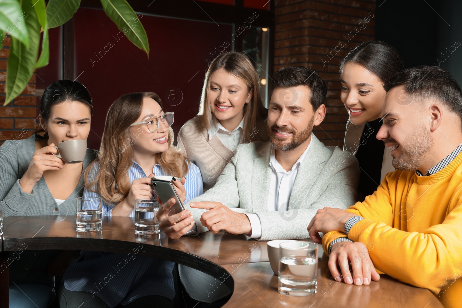 Photo of Handsome man showing something funny in smartphone to his friends in cafe