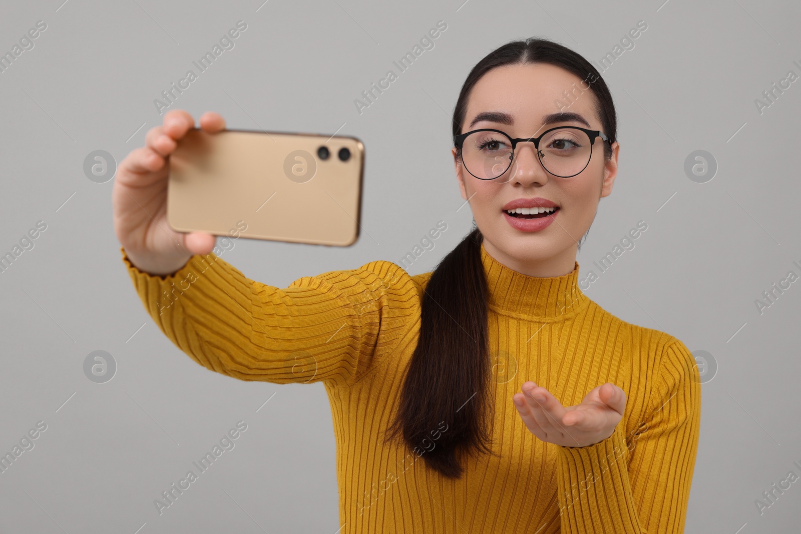 Photo of Smiling young woman taking selfie with smartphone on grey background