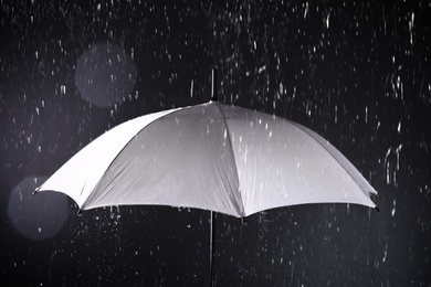 Photo of White umbrella under rain on dark background