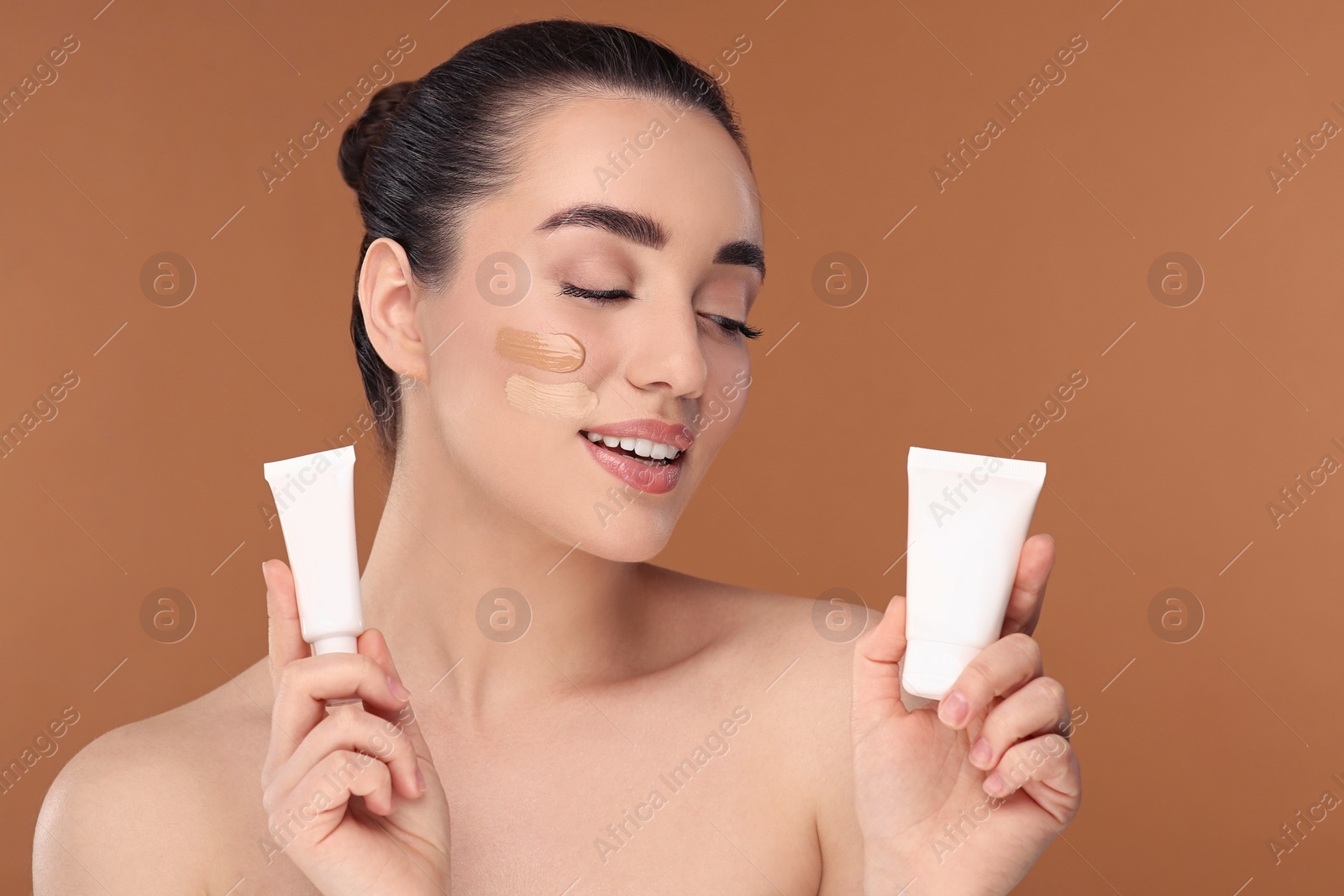 Photo of Woman holding tubes of foundation on brown background