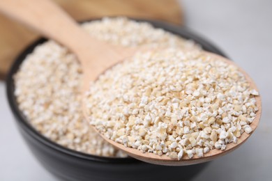 Photo of Dry barley groats in bowl and spoon on light grey table, closeup