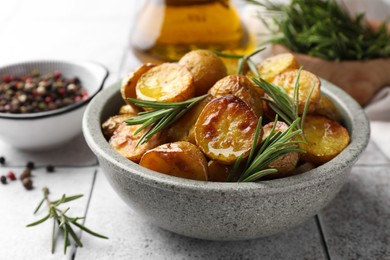 Bowl with tasty baked potato and aromatic rosemary on white tiled table, closeup