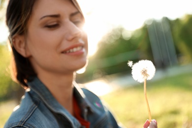 Photo of Young woman with dandelion in park on sunny day. Allergy free concept