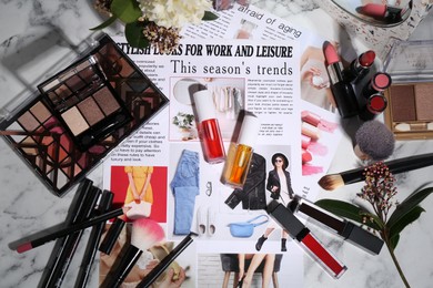 Photo of Bright lip glosses among different cosmetic products and fashion magazine on table, flat lay