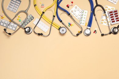 Photo of Stethoscopes and pills on beige background, flat lay. Space for text