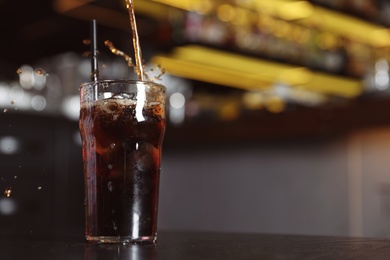 Pouring cola into glass with ice cubes on table indoors. Space for text