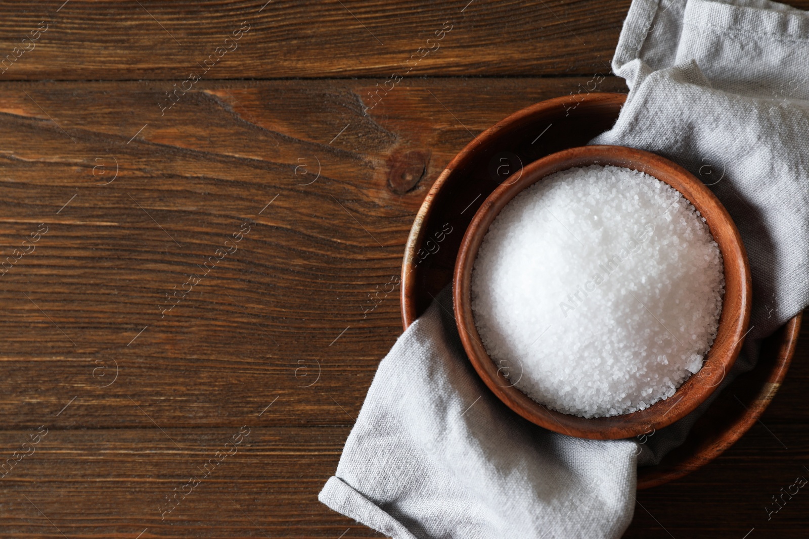 Photo of Organic salt in bowl on wooden table, top view. Space for text