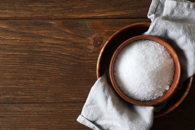 Photo of Organic salt in bowl on wooden table, top view. Space for text