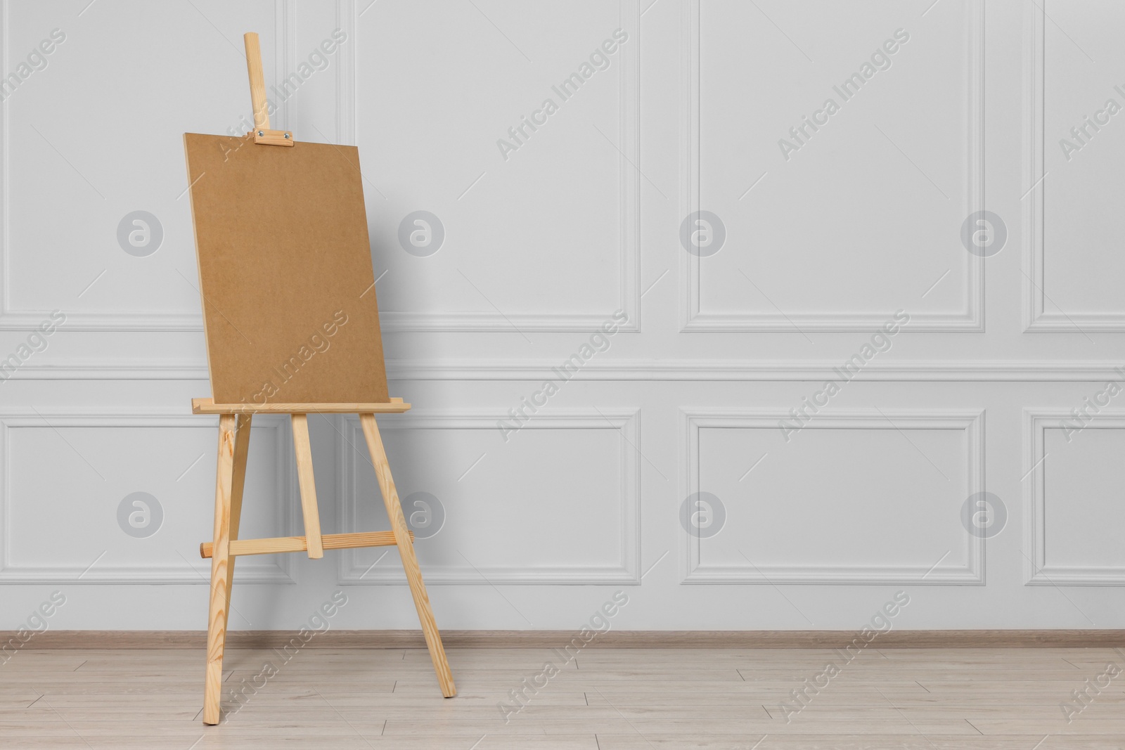 Photo of Wooden easel with blank board near white wall indoors. Space for text