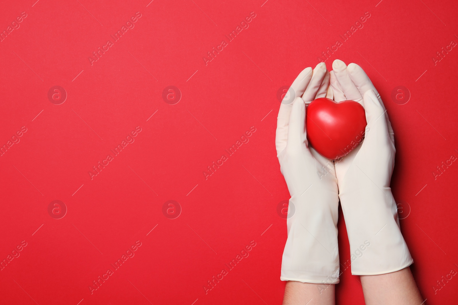 Photo of Doctor in medical gloves holding heart on color background, top view. Space for text