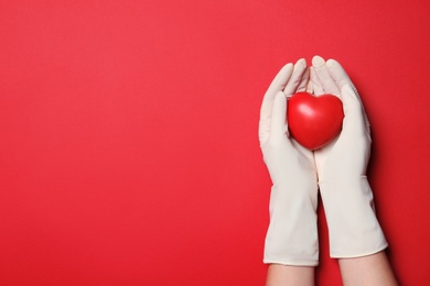 Photo of Doctor in medical gloves holding heart on color background, top view. Space for text