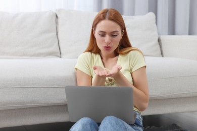 Photo of Woman blowing kiss during video chat via laptop at home. Long-distance relationship