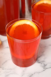 Aperol spritz cocktail and orange slices in glasses on white marble table, closeup