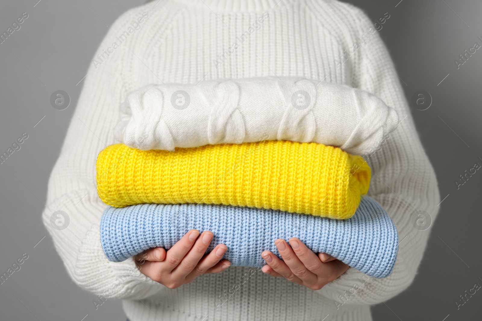 Photo of Woman with stack of knitted sweaters on grey background, closeup