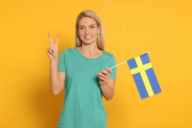 Photo of Woman with flag of Sweden showing V-sign on yellow background