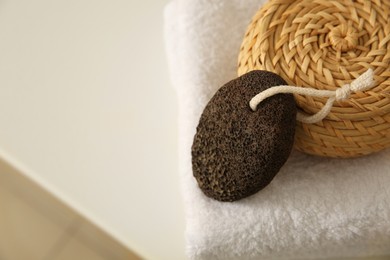 Photo of Pumice stone with wicker basket and soft towel on white table, closeup. Space for text