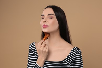 Photo of Beautiful woman applying makeup on light brown background