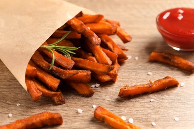 Photo of Paper bag with tasty sweet potato fries and sauce on wooden table, closeup