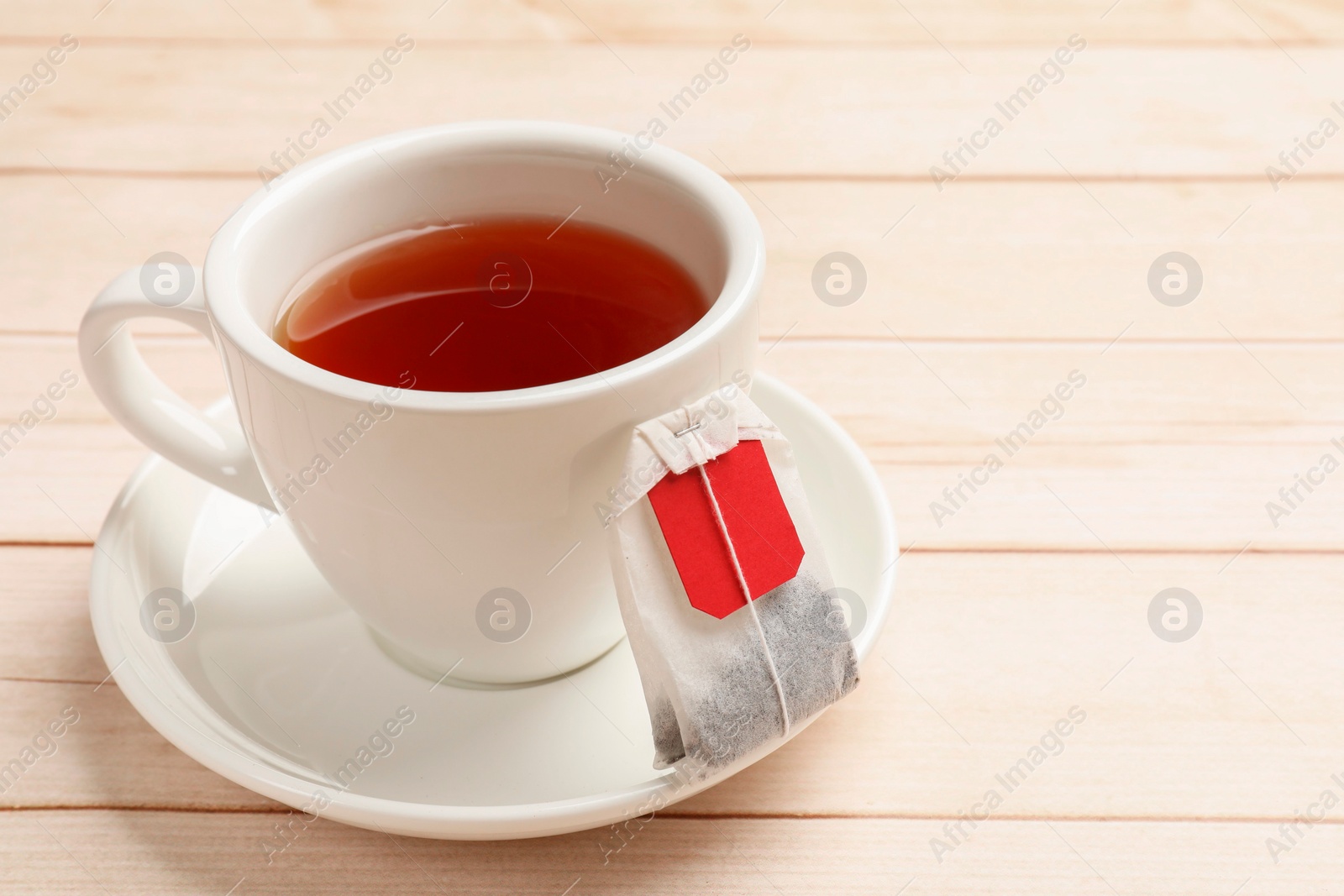 Photo of Tea bag and cup of hot beverage on light wooden table, closeup. Space for text