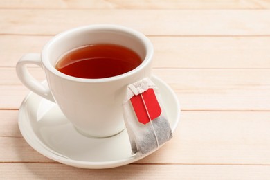 Tea bag and cup of hot beverage on light wooden table, closeup. Space for text