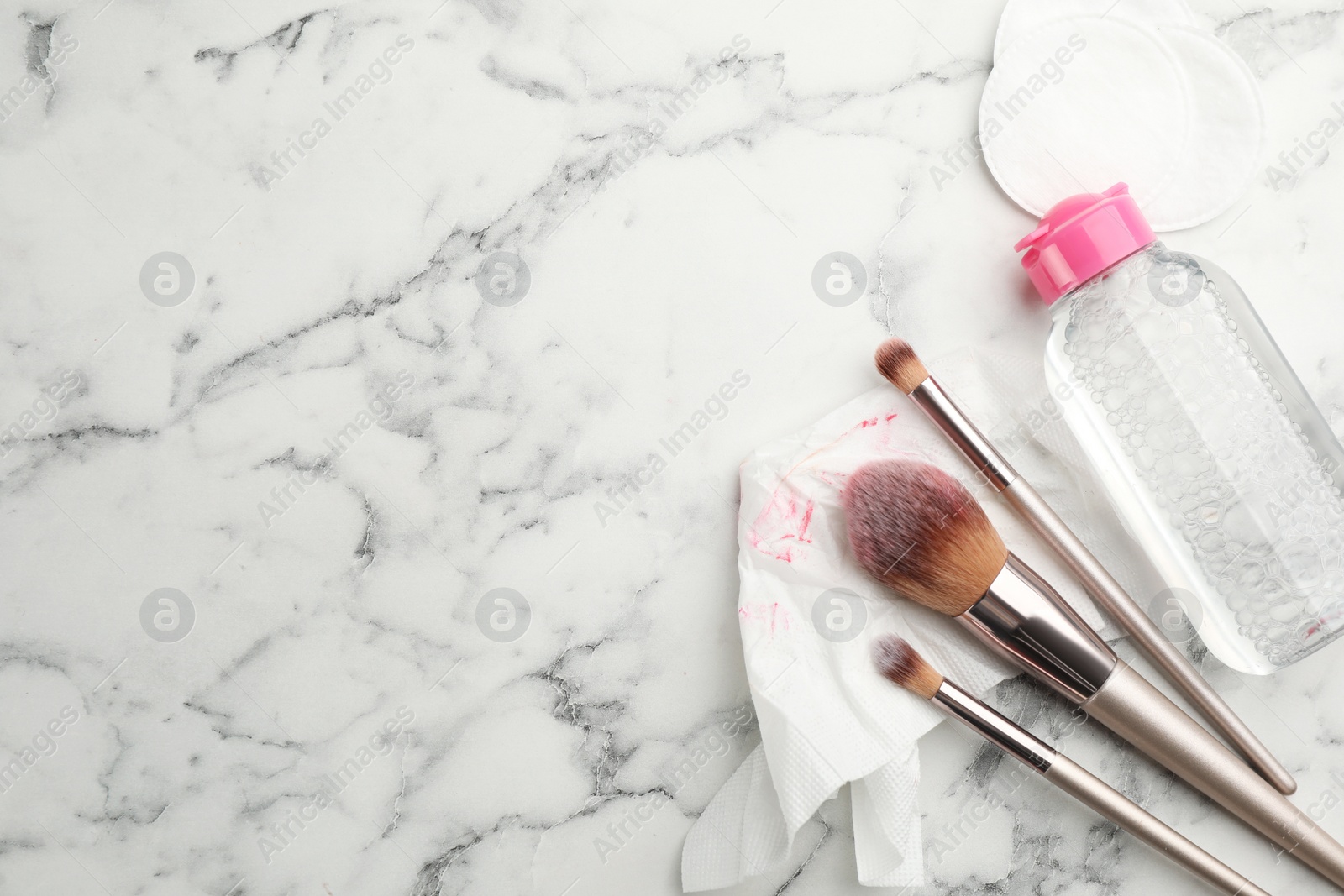 Photo of Dirty tissue, cotton pads, brushes and micellar cleansing water on white marble background, flat lay. Space for text