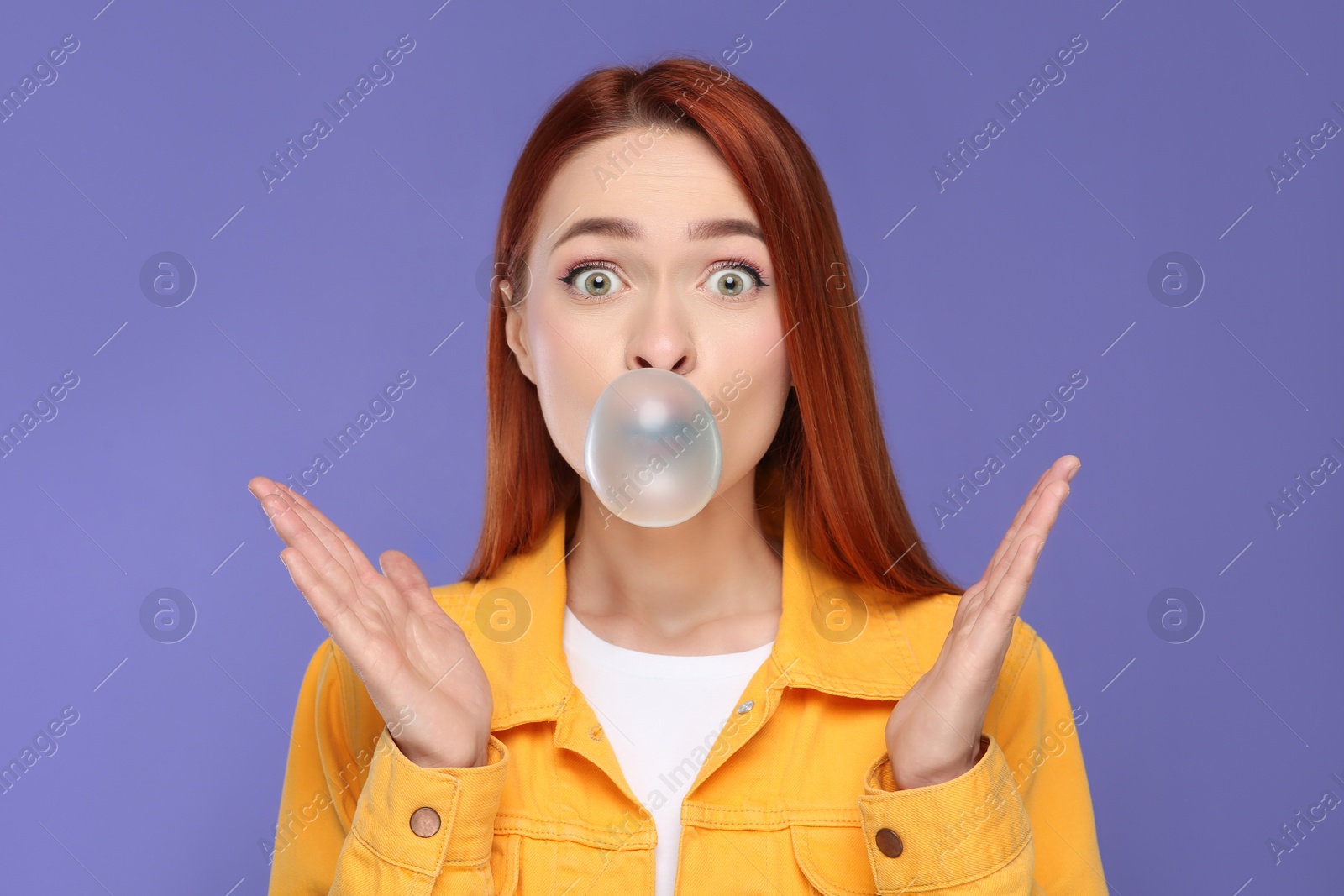 Photo of Surprised woman blowing bubble gum on purple background