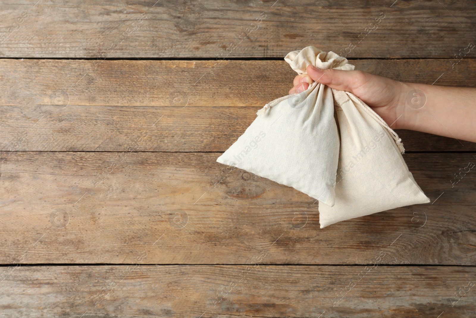 Photo of Woman holding full cotton eco bags on wooden background, closeup. Space for text