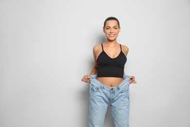 Photo of Slim woman in oversized jeans on light background. Weight loss