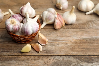 Photo of Fresh organic garlic in wicker basket on wooden table. Space for text