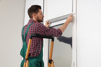 Photo of Worker in uniform installing roller window blind indoors