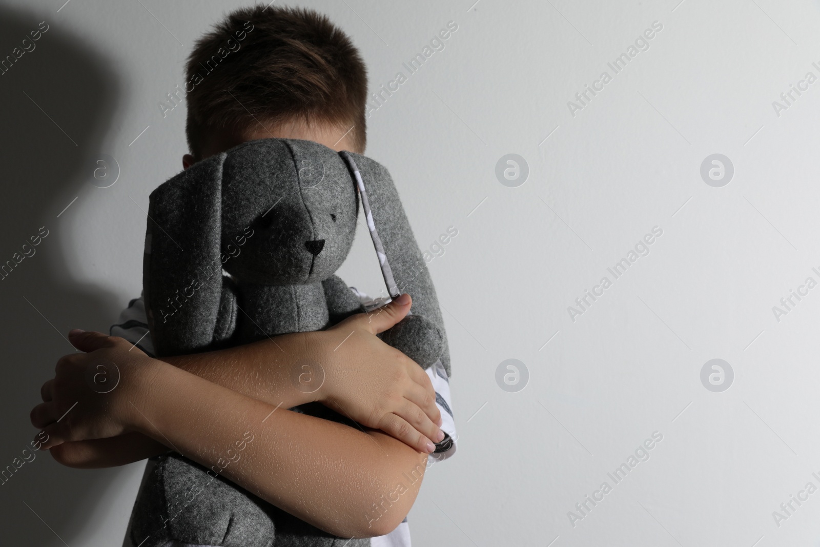 Photo of Little boy with toy near white wall, space for text. Domestic violence concept