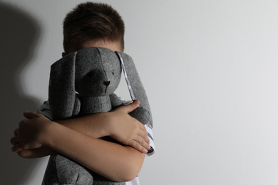 Little boy with toy near white wall, space for text. Domestic violence concept