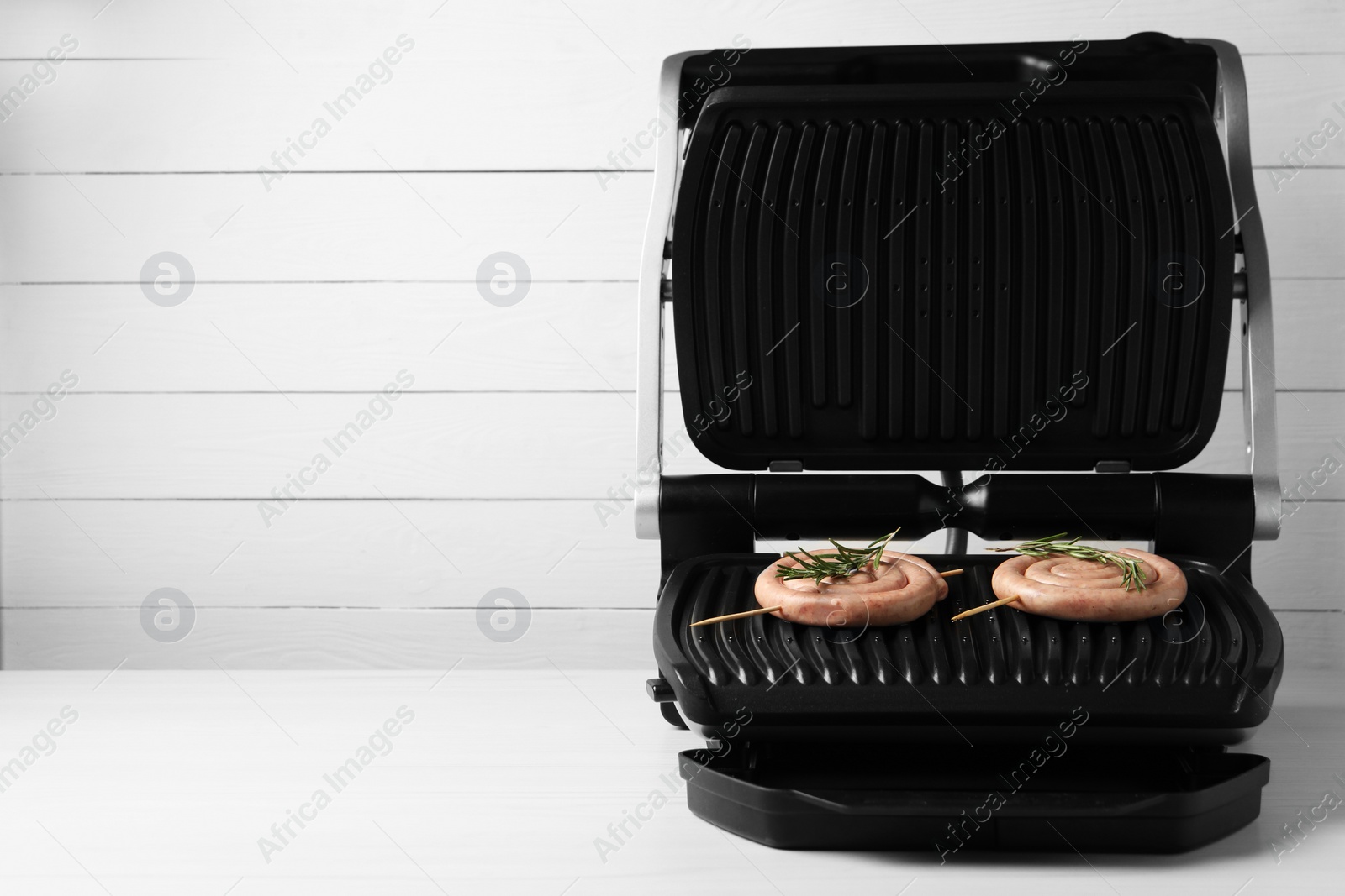 Photo of Electric grill with homemade sausages and rosemary on wooden table. Space for text