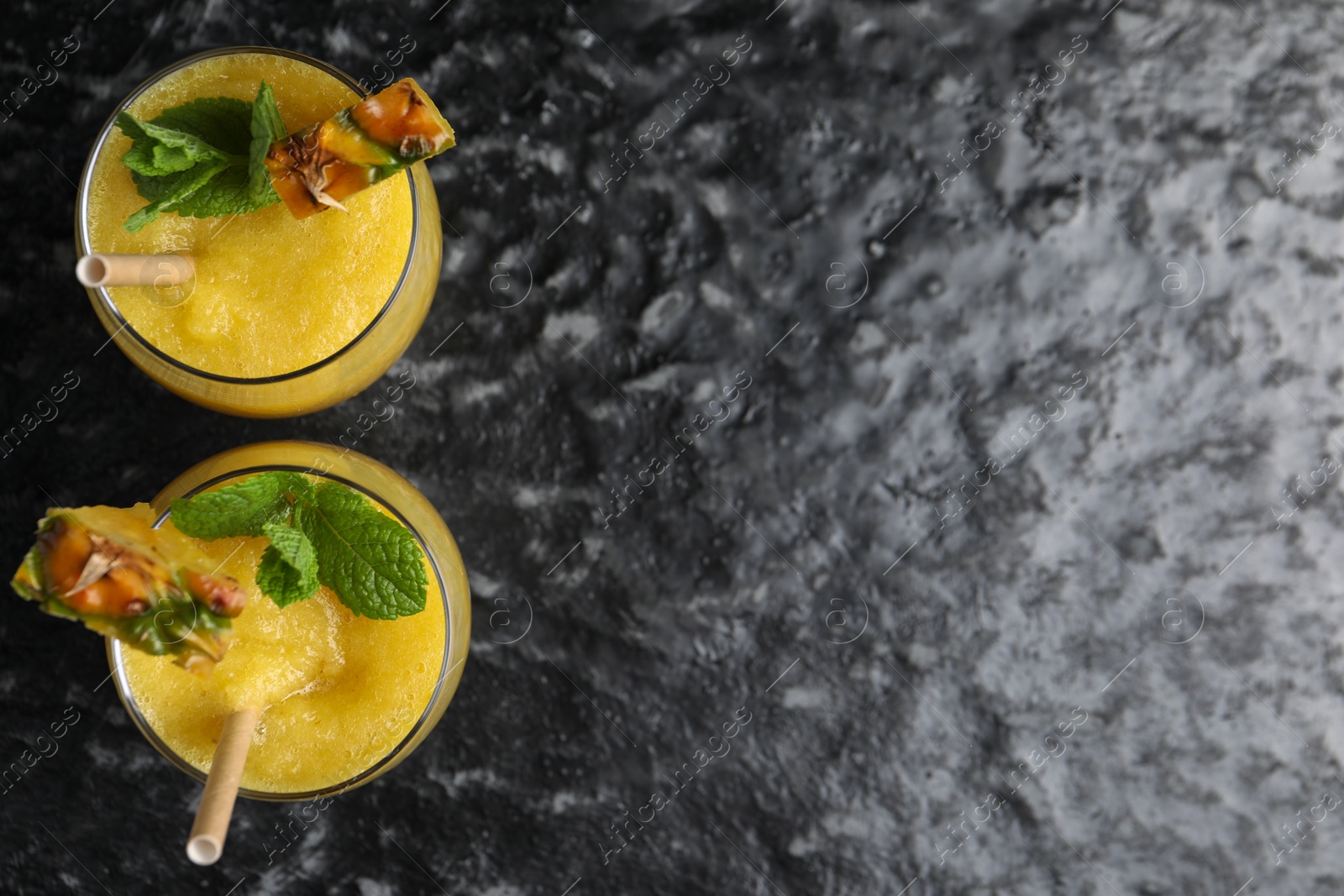 Photo of Tasty pineapple smoothie in glasses on black textured table, top view. Space for text