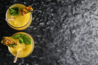 Photo of Tasty pineapple smoothie in glasses on black textured table, top view. Space for text