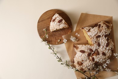 Delicious cut Italian Easter dove cake (traditional Colomba di Pasqua) and flowering branches on beige table, flat lay. Space for text