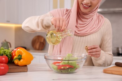 Muslim woman making delicious salad with vegetables at white table in kitchen, closeup