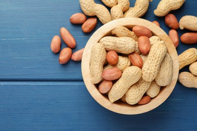 Photo of Fresh unpeeled peanuts in bowl on blue wooden table, top view. Space for text