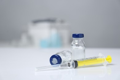 Photo of Syringe and vials on white table. Space for text