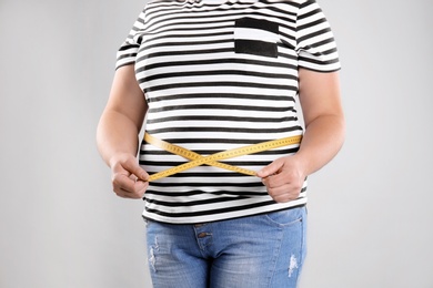 Photo of Fat woman with measuring tape on grey background, closeup. Weight loss